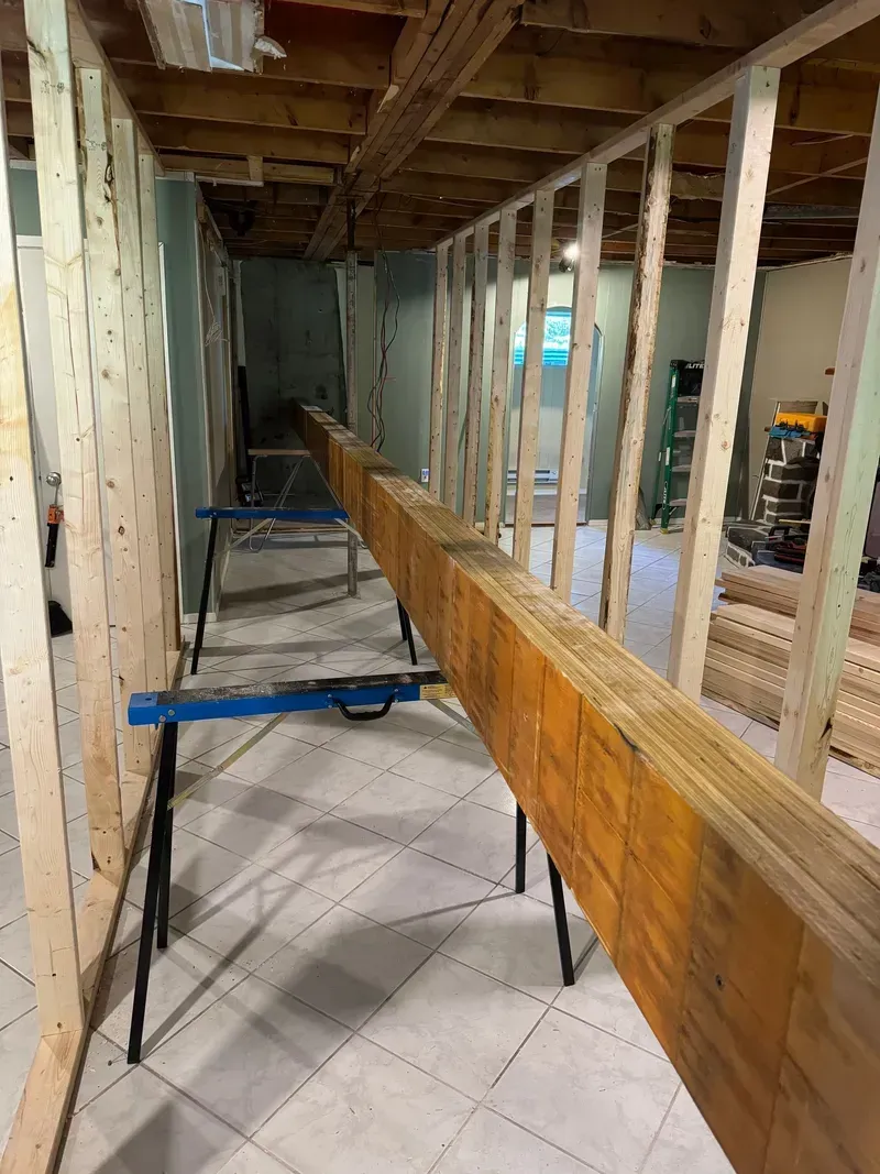 Une longue poutre en bois repose sur un établi dans une pièce en construction.