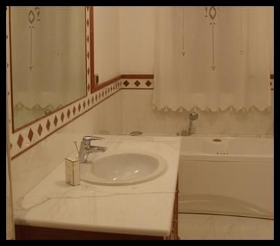 Bagno con lavandino, vasca e pareti bianchi; bordo piastrellato rosso.