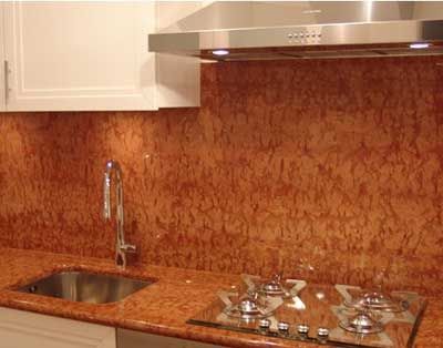 Cucina con piano di lavoro e paraschizzi in granito arancione, lavello in acciaio inossidabile e piano cottura.