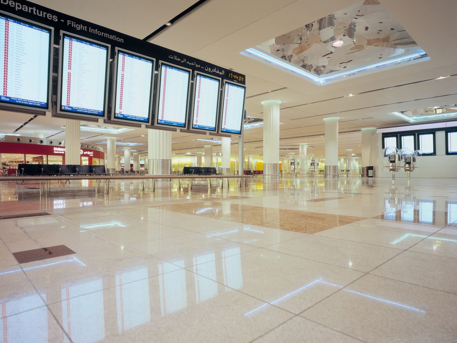Un terminal aeroportuale vuoto e ben illuminato, con schermi informativi sui voli in alto e pavimenti piastrellati.
