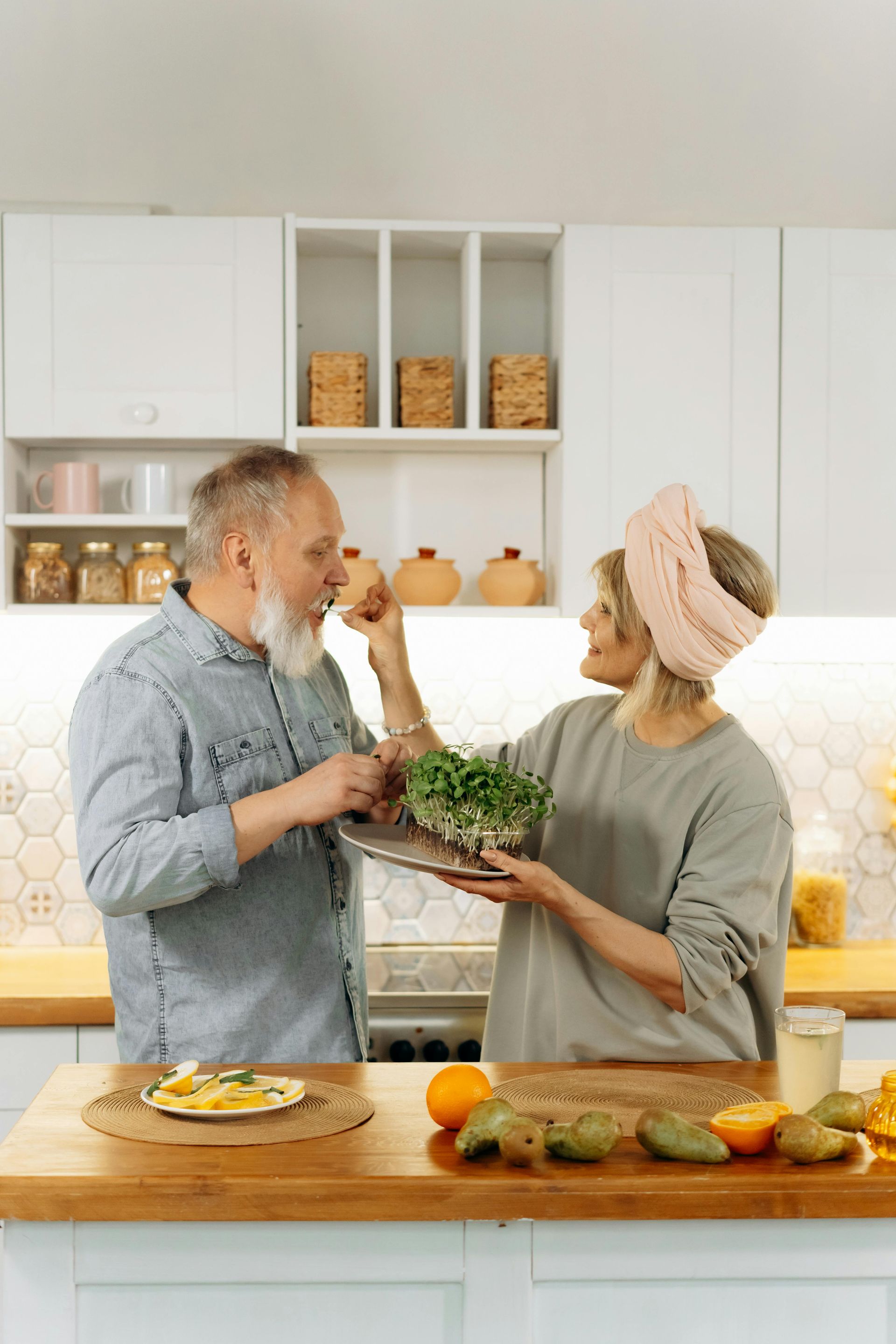 A man and a woman are standing in a kitchen holding a tray of food.