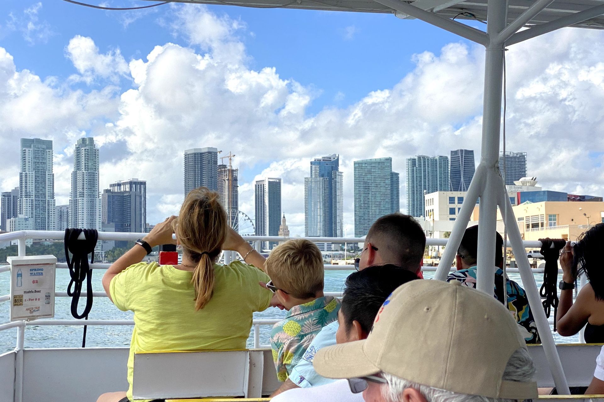 A water taxi cruising through the ocean with some buildings in the background.