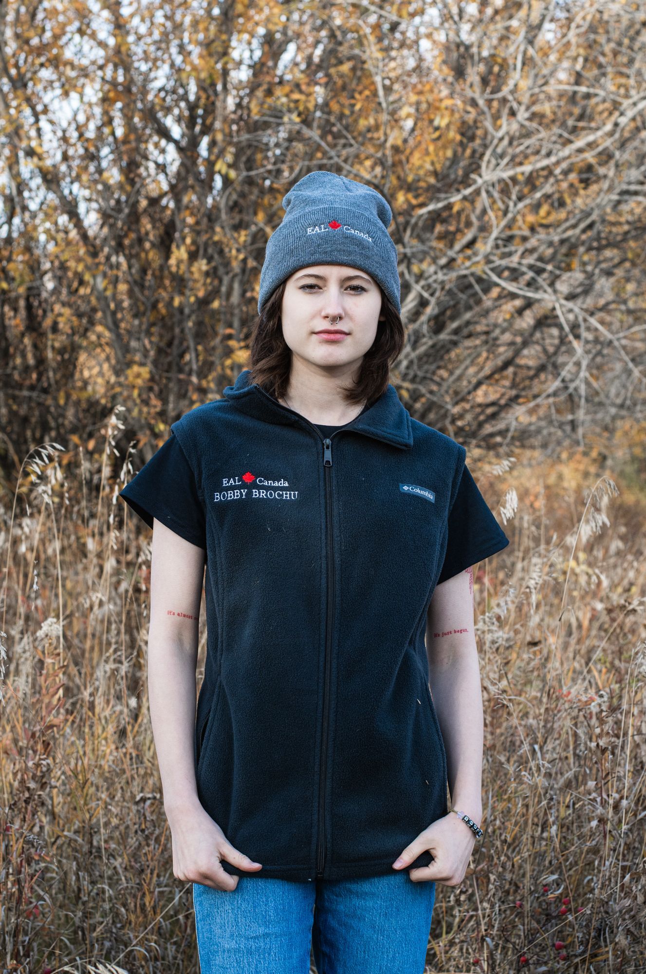 A woman wearing a black vest and a gray hat is standing in a field.