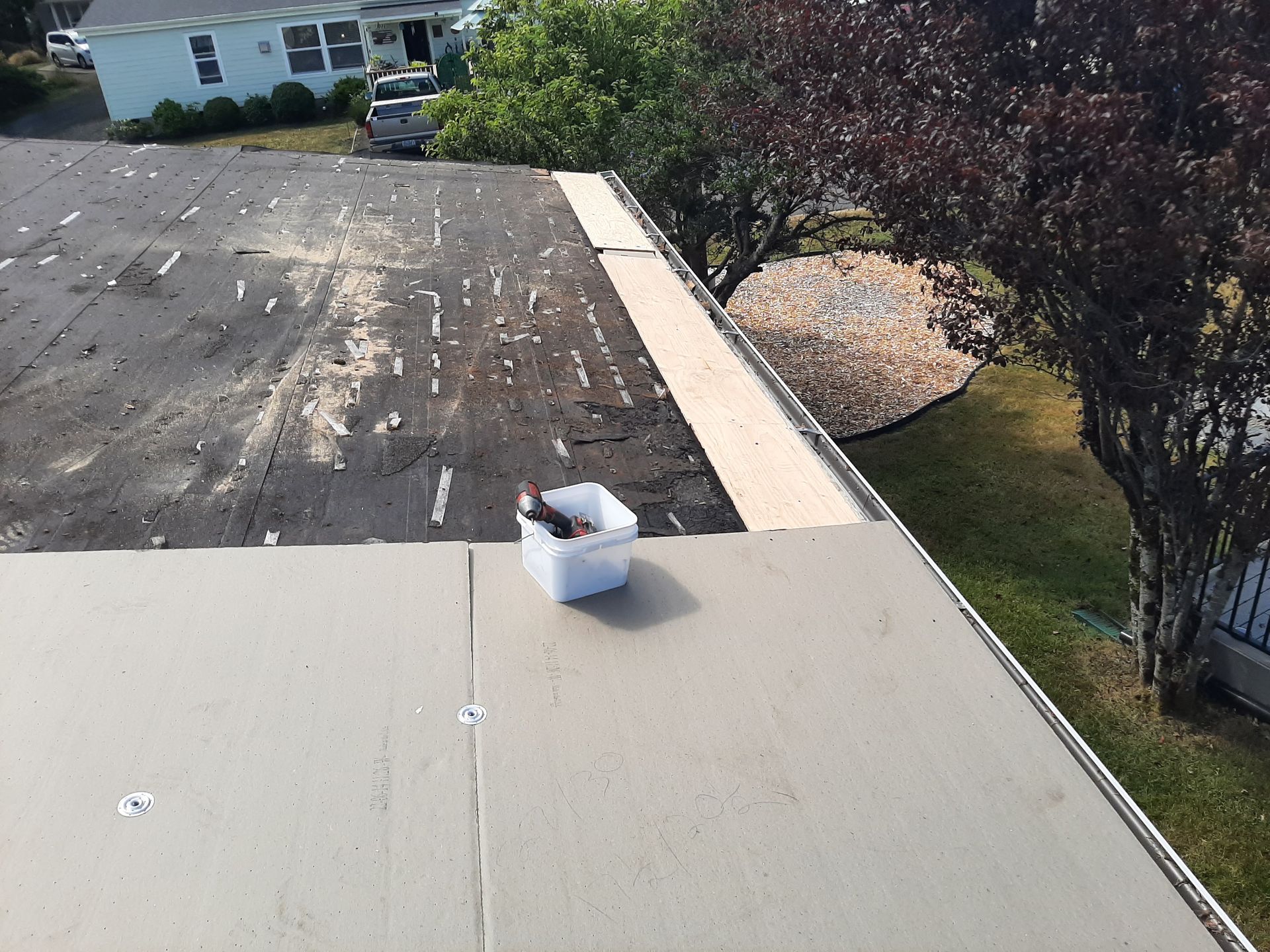 Flat roof partially repaired with new material. White bucket with tools. Bright outdoors.