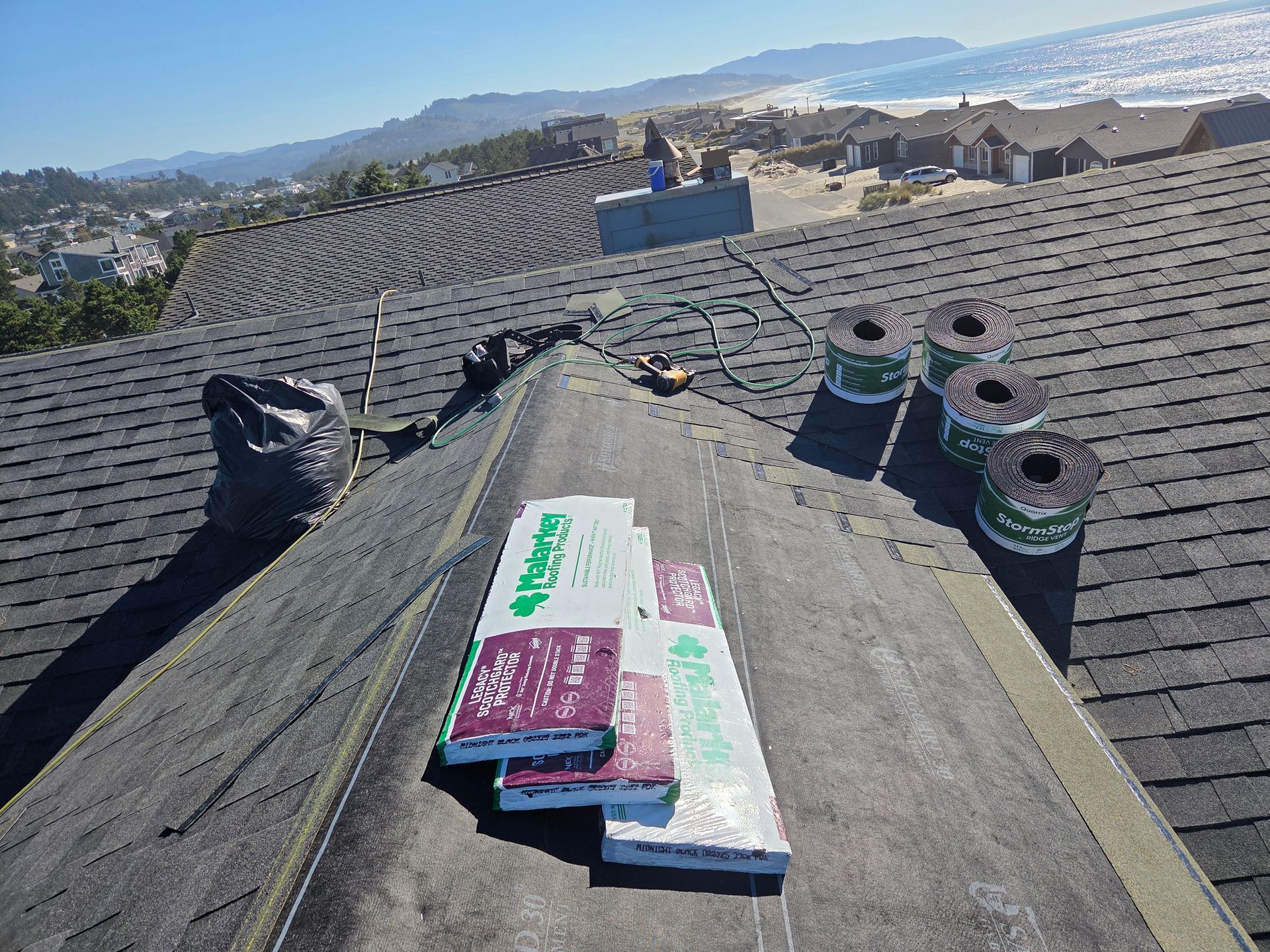 Rooftop with materials for repairs, overlooking a coastal view. Black shingles, green and white insulation, coils.