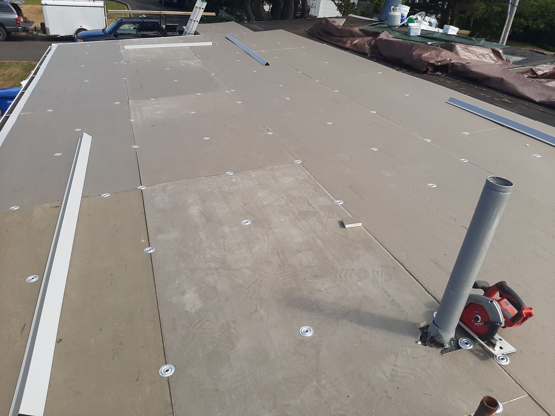 Flat roof under construction with gray insulation panels, tools, and PVC pipes.