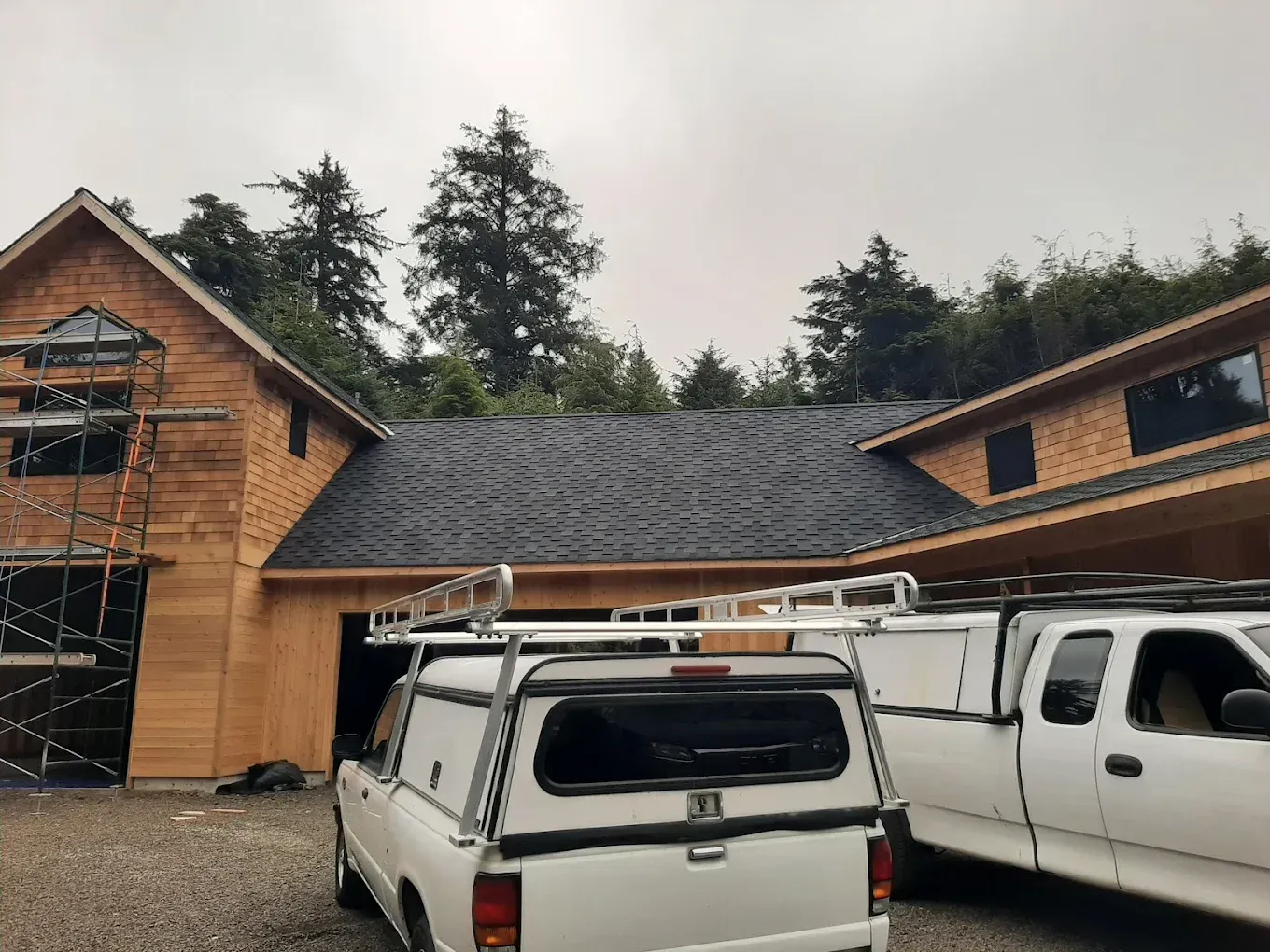 Two white trucks parked in front of a wood-sided house with a dark roof under an overcast sky.