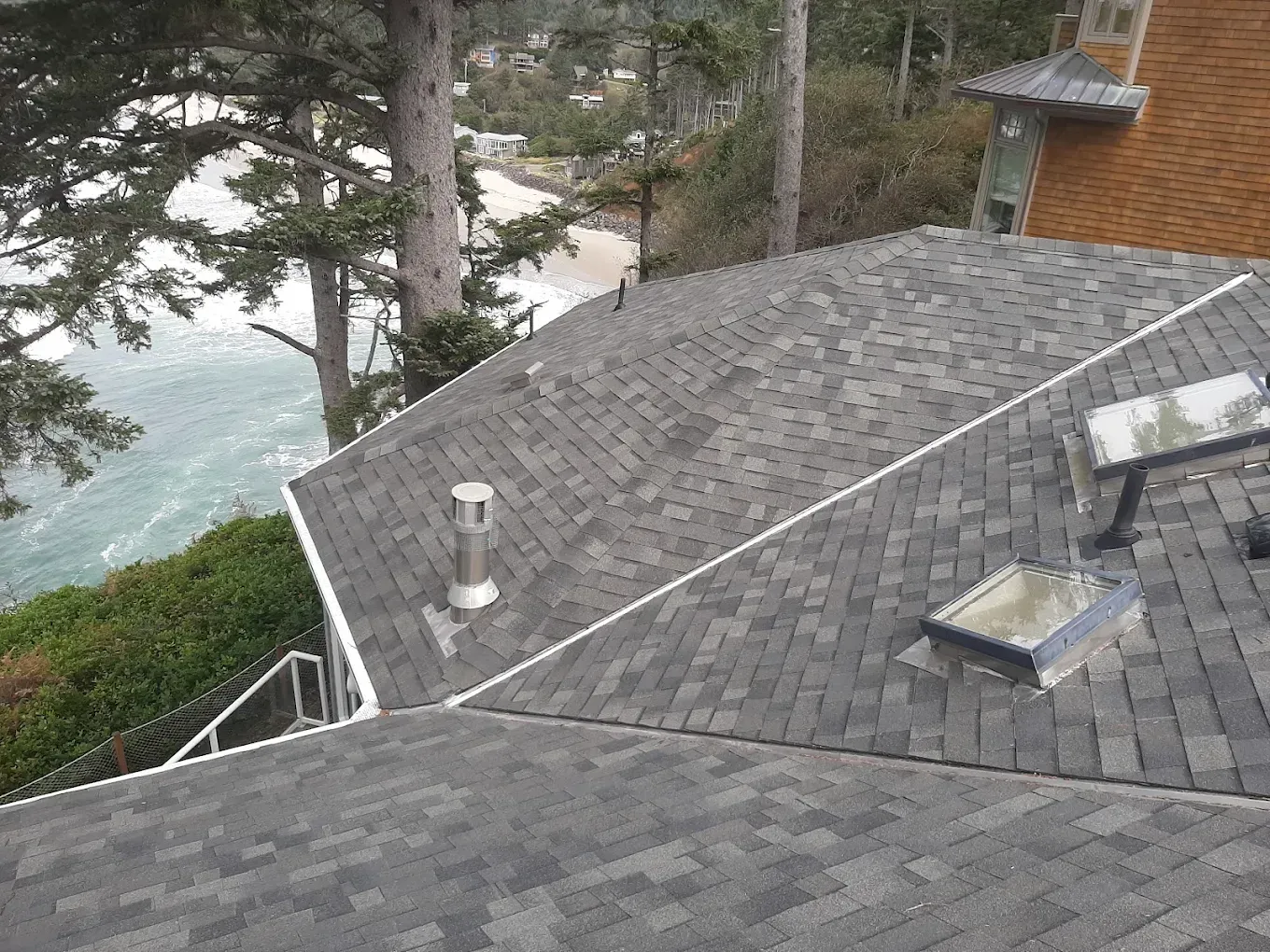 Gray shingled roof with a chimney and skylight, overlooking a beach and ocean.