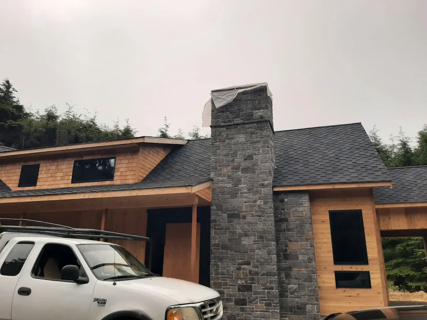 A stone chimney on a house with a dark roof; a white truck parked nearby.