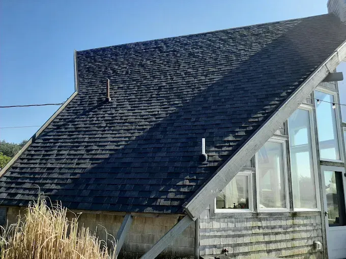 A dark shingle roof on a light-colored wooden building with large windows on a sunny day.