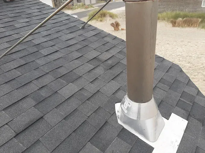 Dark gray asphalt shingle roof with a vent pipe and a white flashing.