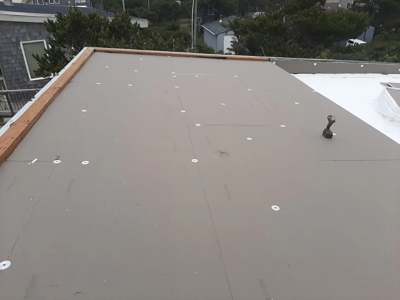 Flat, gray roof with white fasteners, a vent, and trees in the background.
