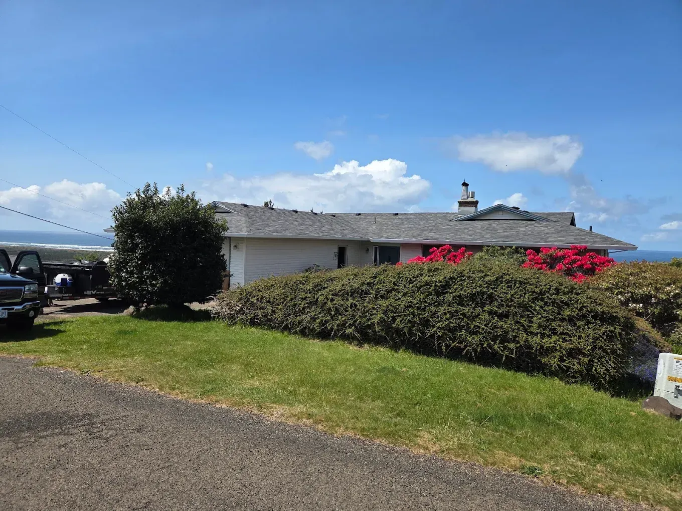 House with green lawn, bushes with red flowers, gray roof, blue sky with clouds.