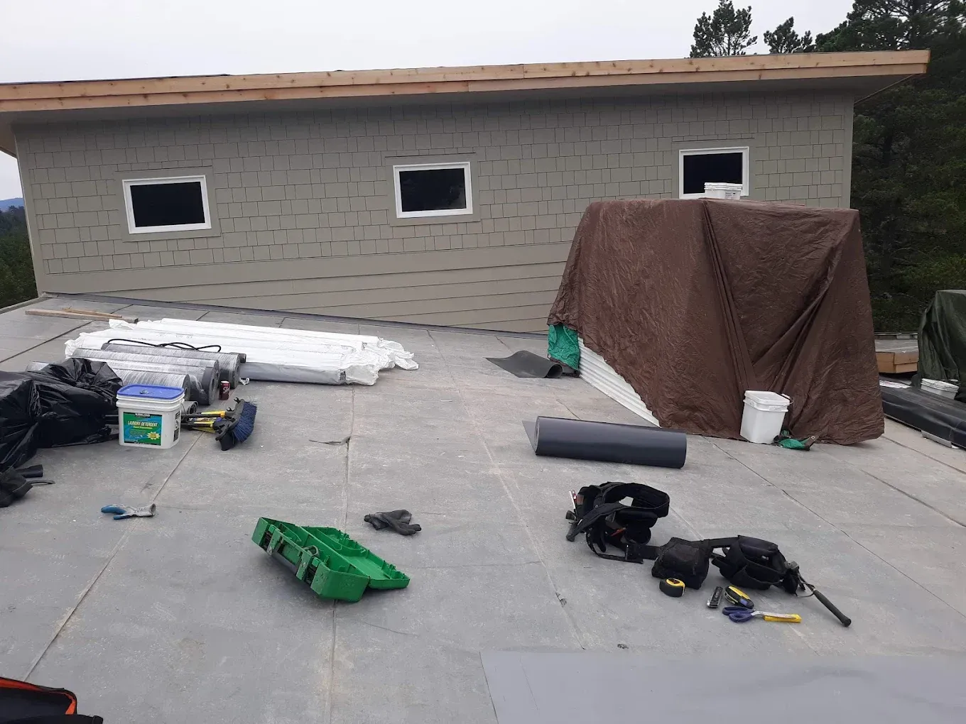 Construction site with tools and materials on flat roof of a building with three windows.