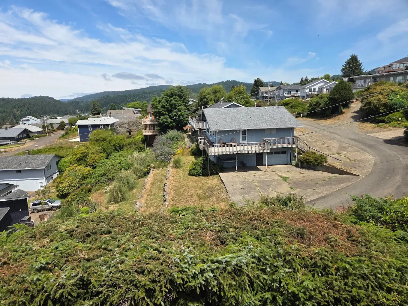 A two-story house on a hillside with a blue sky and other houses visible in the background.