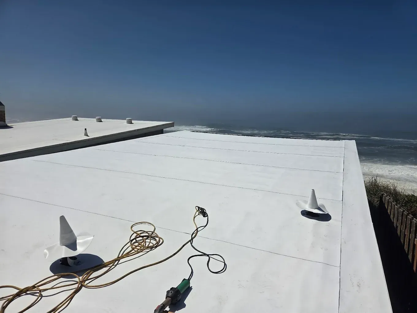 White flat roof overlooking the ocean. Tools and equipment on the roof under a clear blue sky.