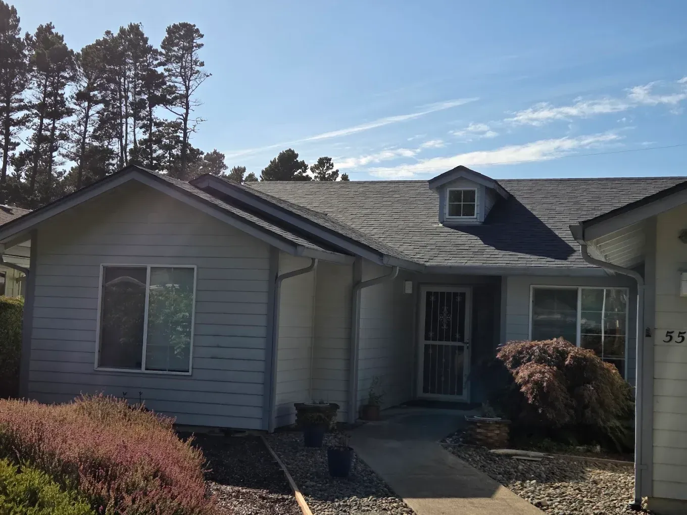 Light blue house with a dormer, blue sky, and landscaping.
