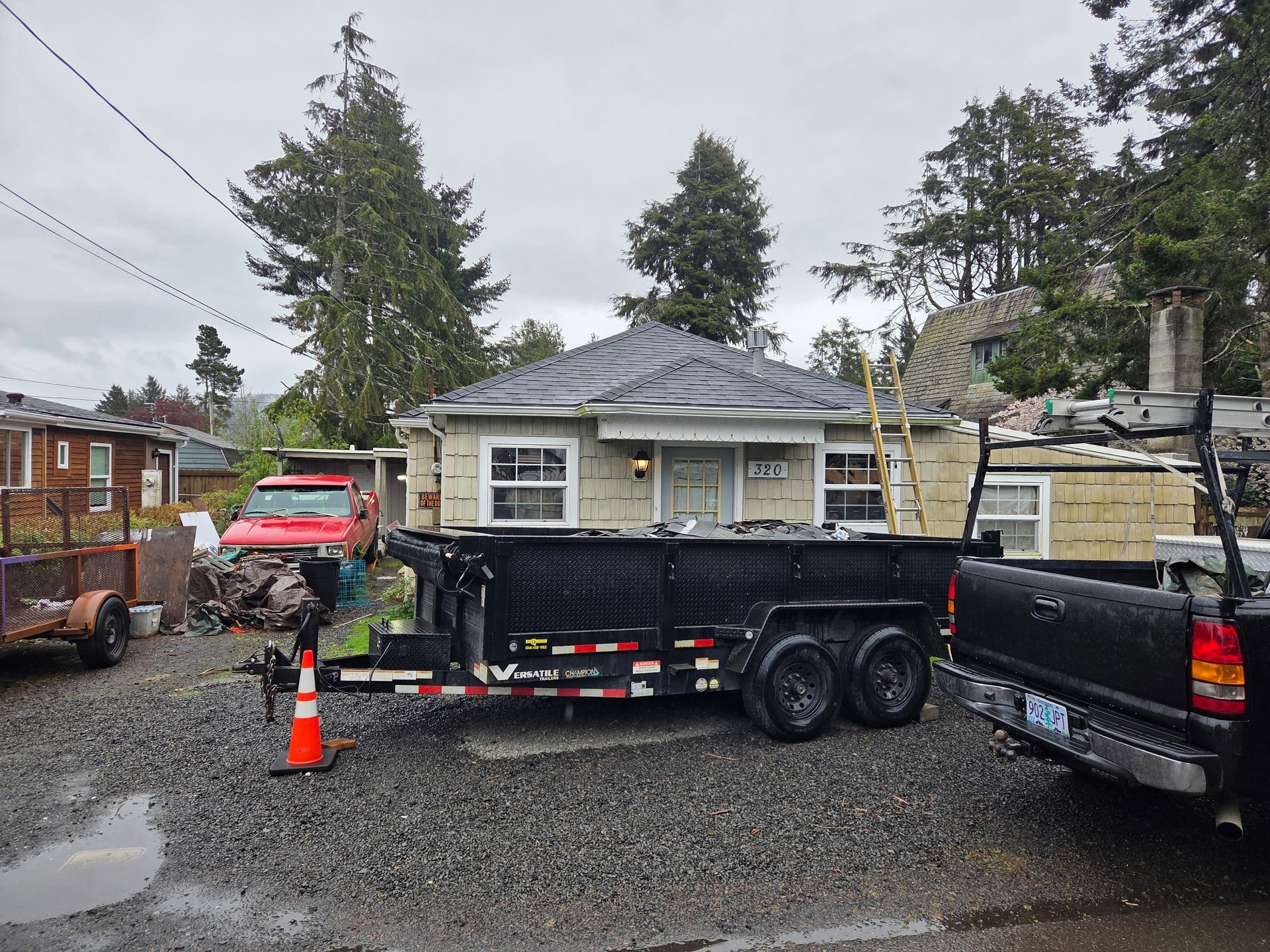 A small house undergoing renovation, with a trailer and trucks in the gravel driveway.
