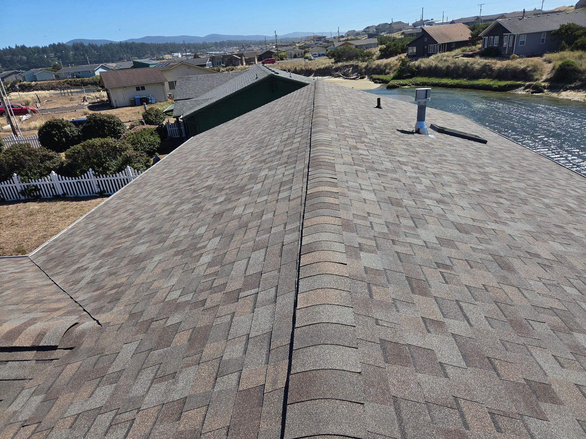 View of a multi-toned, shingled roof with a centered ridge, overlooking a coastal town and waterway.