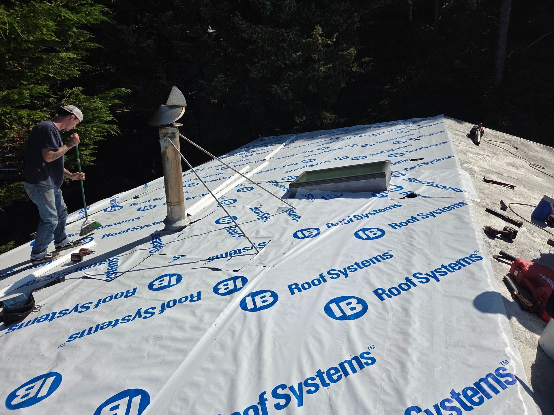 Man on a roof installing roofing material, with a chimney and skylight visible.