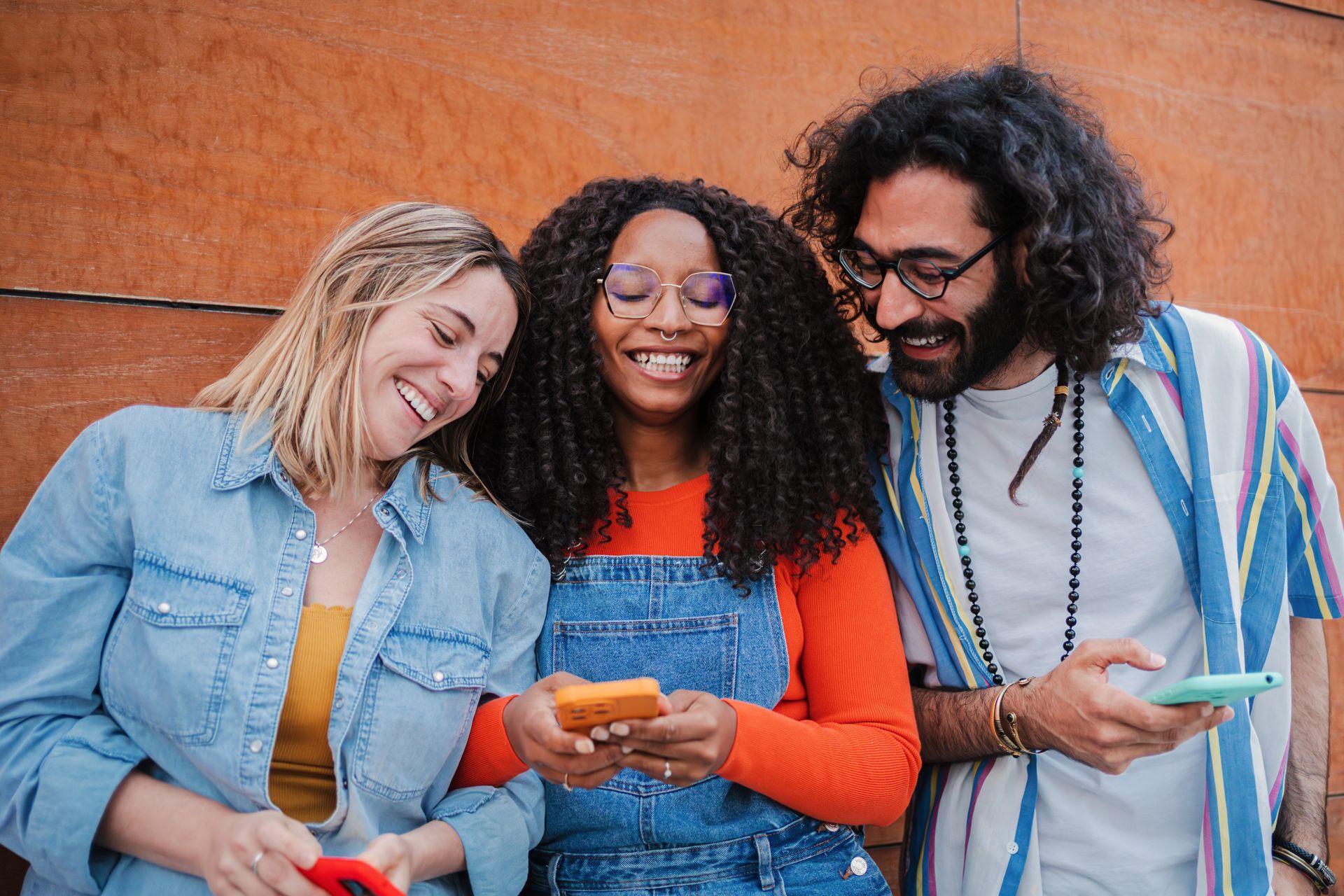 A group of young people are standing next to each other looking at their phones.