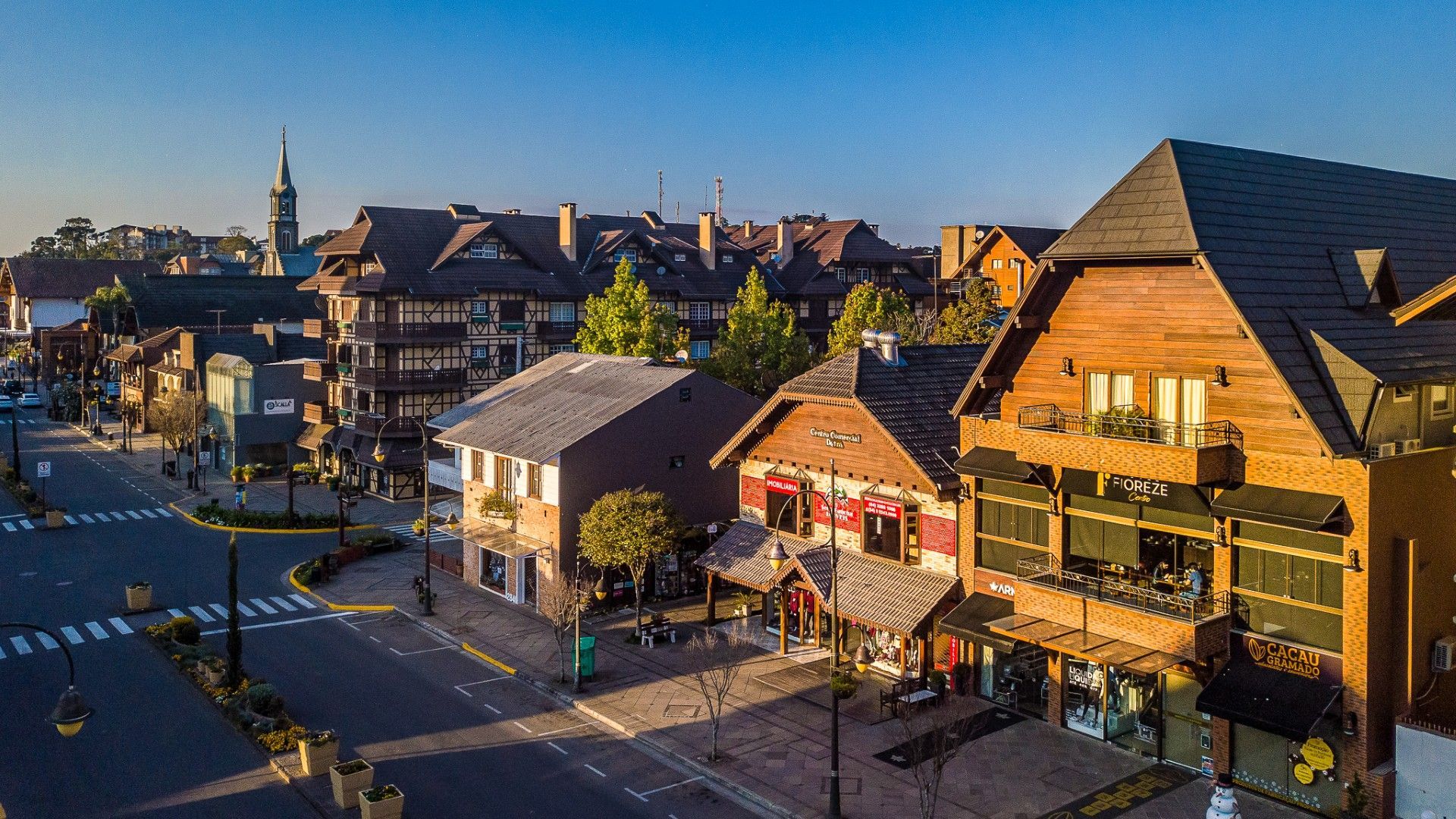 Vista aérea ensolarada de uma rua de pedestres ladeada por edifícios de madeira em estilo alpino e pequenas lojas em uma vila europeia.