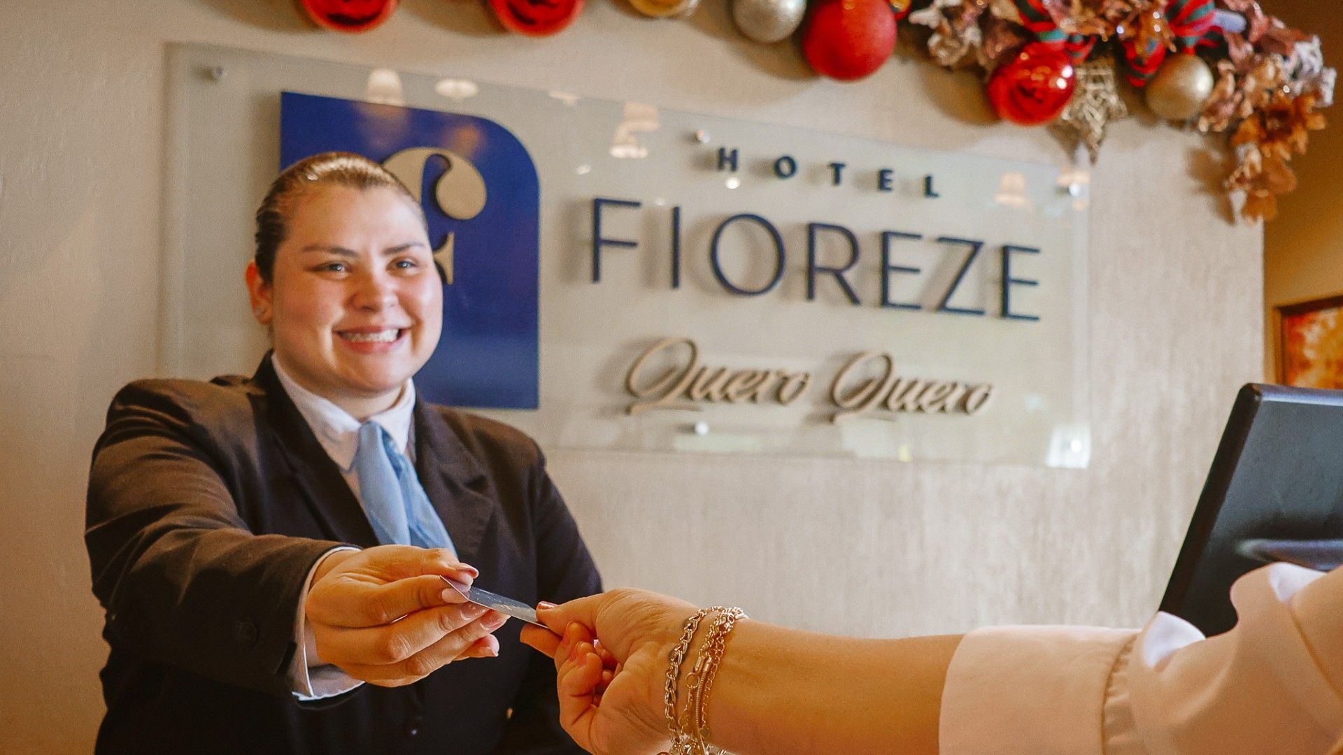 Uma recepcionista sorridente entrega um cartão-chave a um hóspede na recepção do Hotel Fioreze.