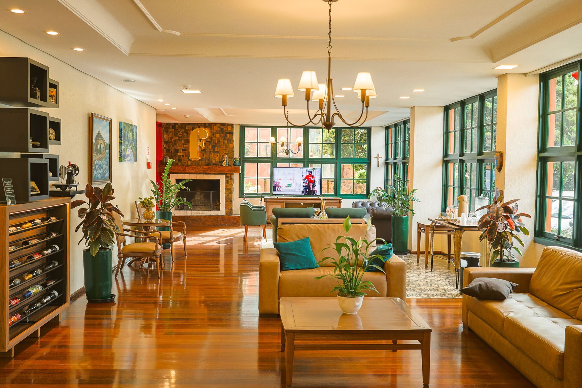 Uma sala de estar aconchegante com piso de madeira, sofás bege, uma mesa de centro, uma lareira e um grande lustre.