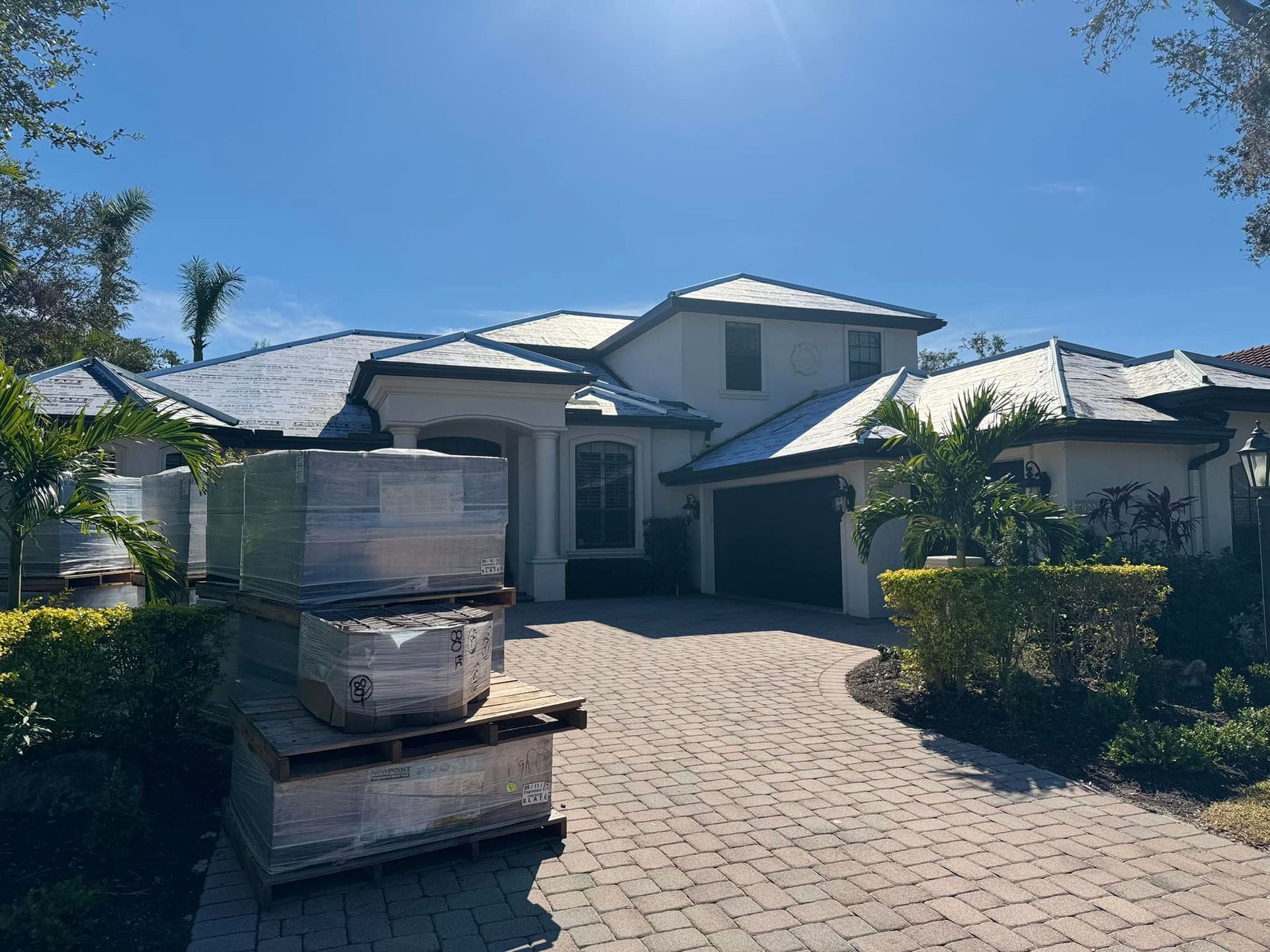 A large white house with a brick driveway and a stack of pallets in front of it.