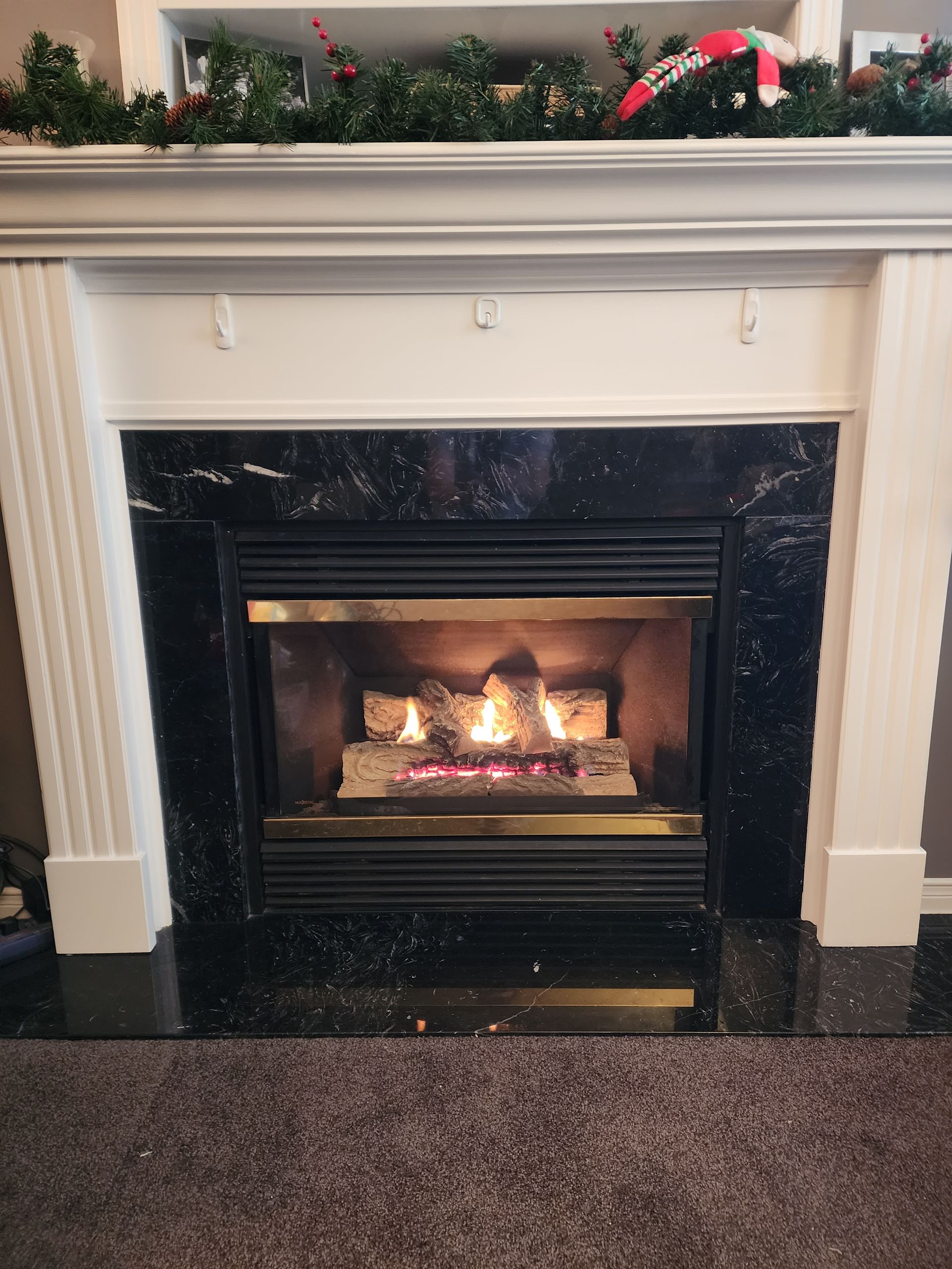 Fireplace with black marble surround, burning logs, decorated mantel, and garland.