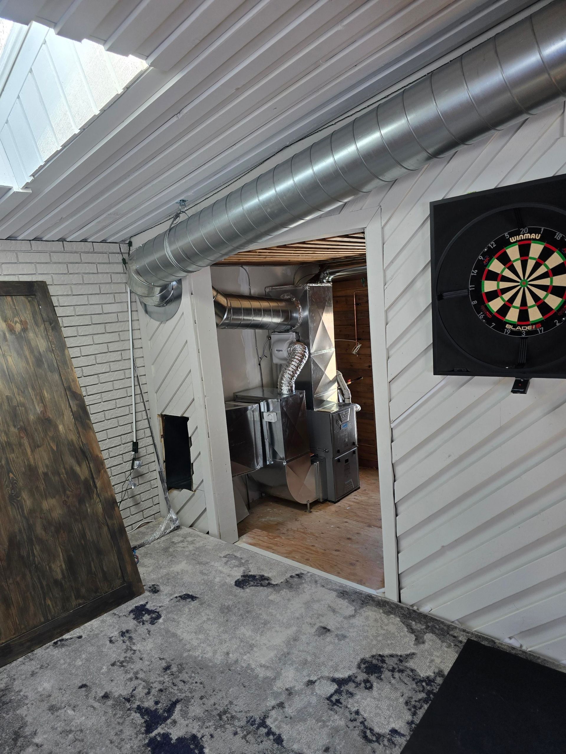 Dartboard, ductwork, and furnace inside a white-walled room with a gray floor.