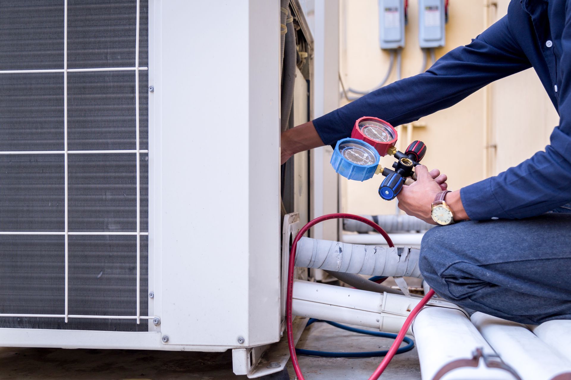 A man is kneeling down and working on an air conditioner.