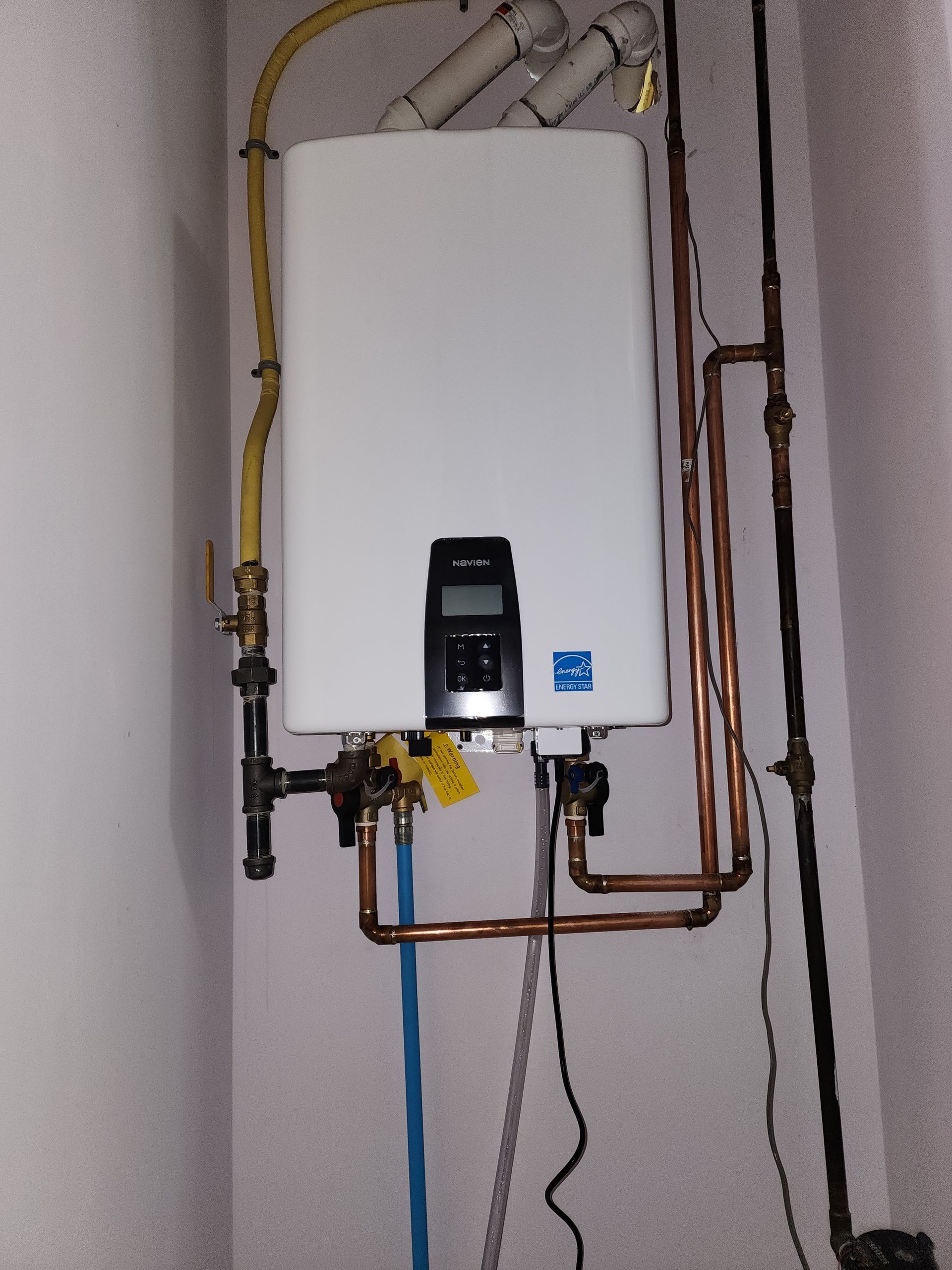 White tankless water heater mounted on a wall with copper and black pipes.