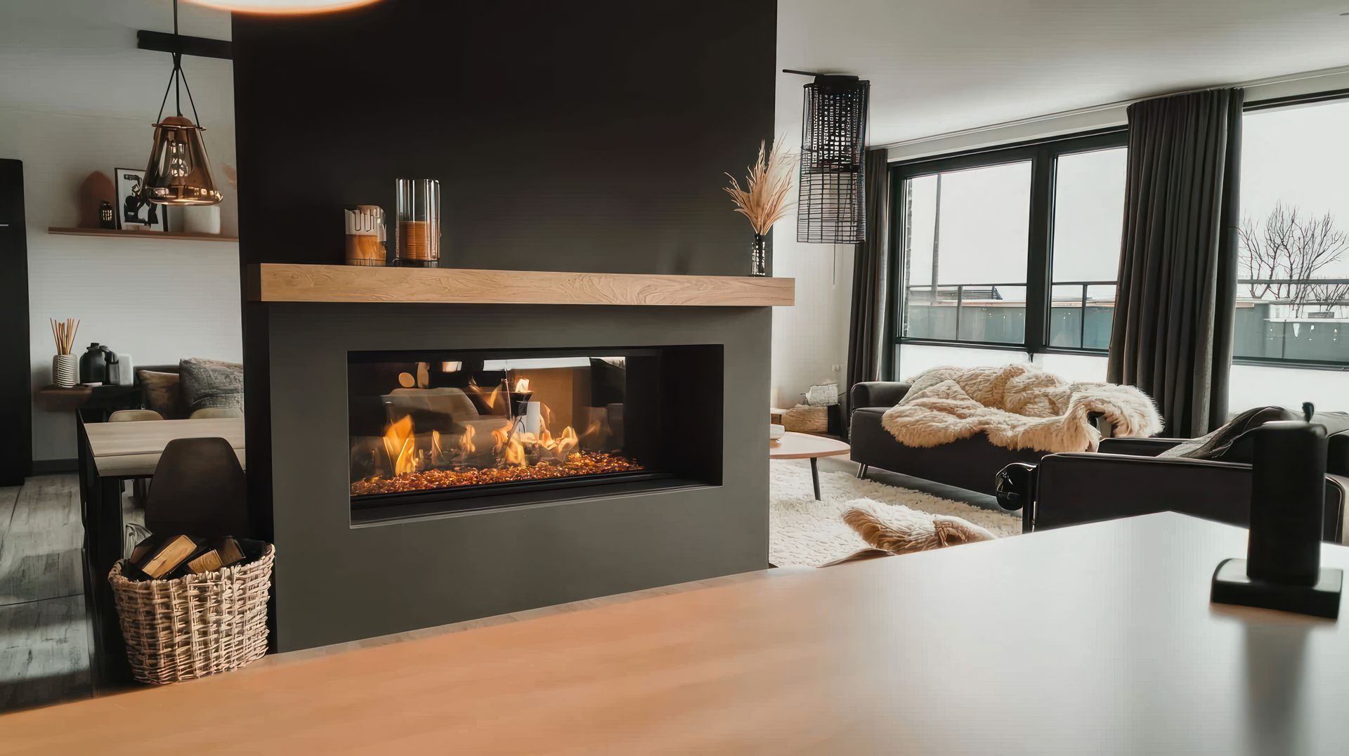 A modern living room with a black fireplace, a light wood mantel, and a cozy seating area with dark furniture.