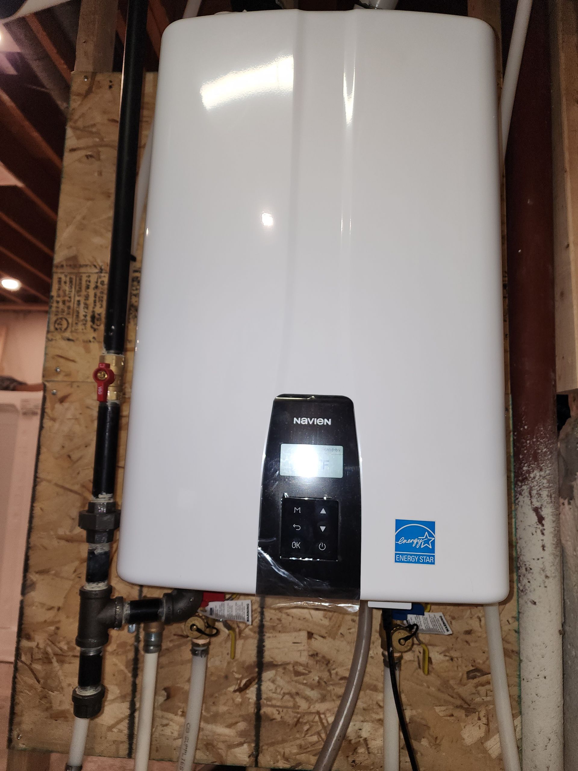 A white water heater is hanging on a wall next to pipes.