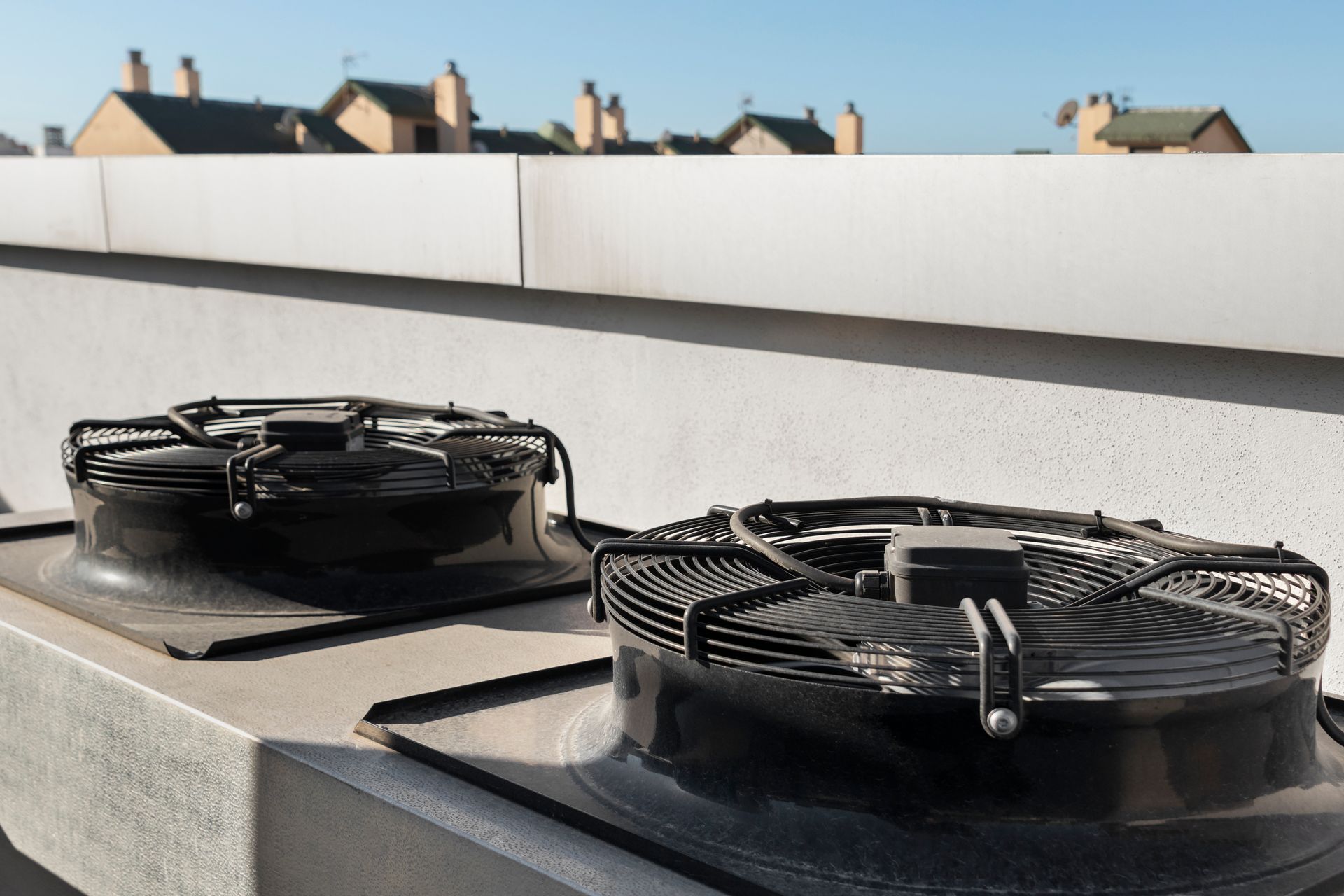 Two industrial cooling fans mounted on a rooftop with houses visible in the background under a clear sky.