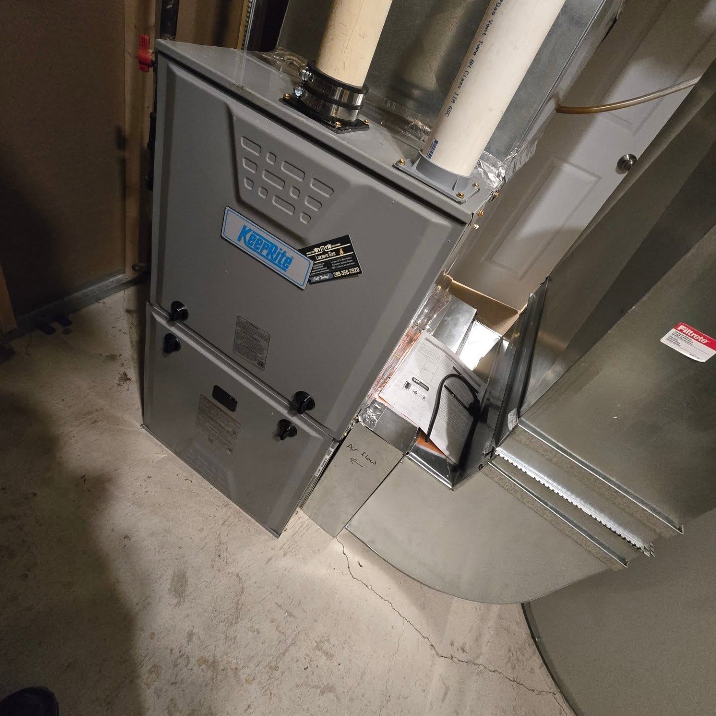 A gray furnace in a basement setting with ductwork and piping.