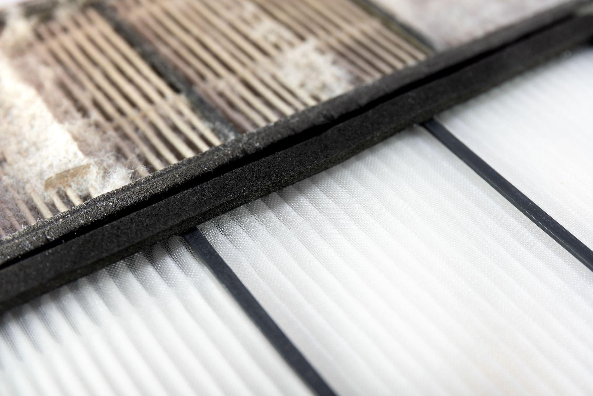 A dirty, gray air filter section sits next to a clean, white pleated filter, showing the contrast between the two.