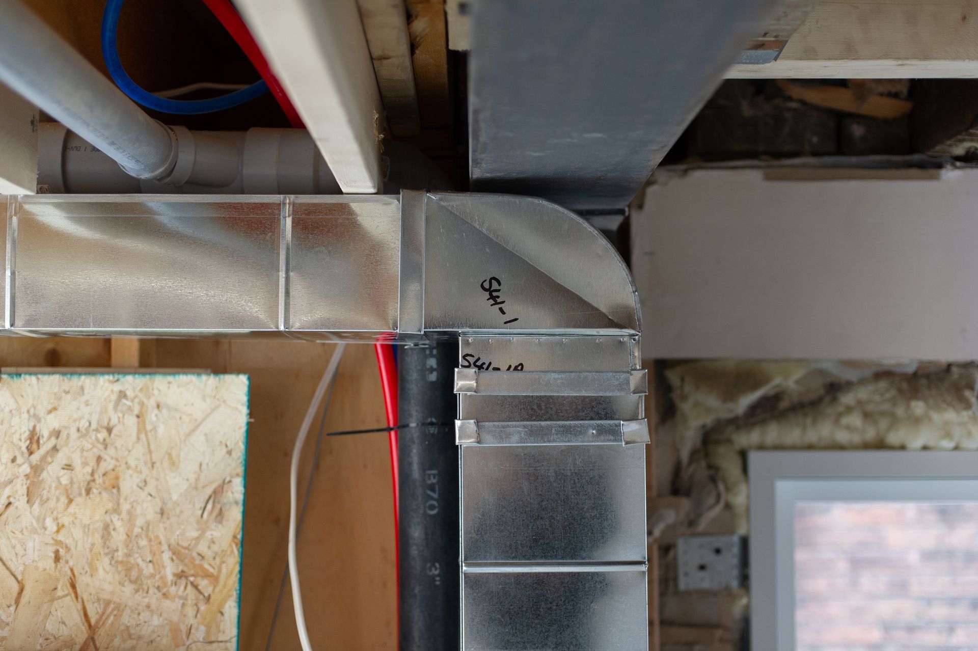 Metal ductwork in a basement ceiling, with exposed wood and pipes.