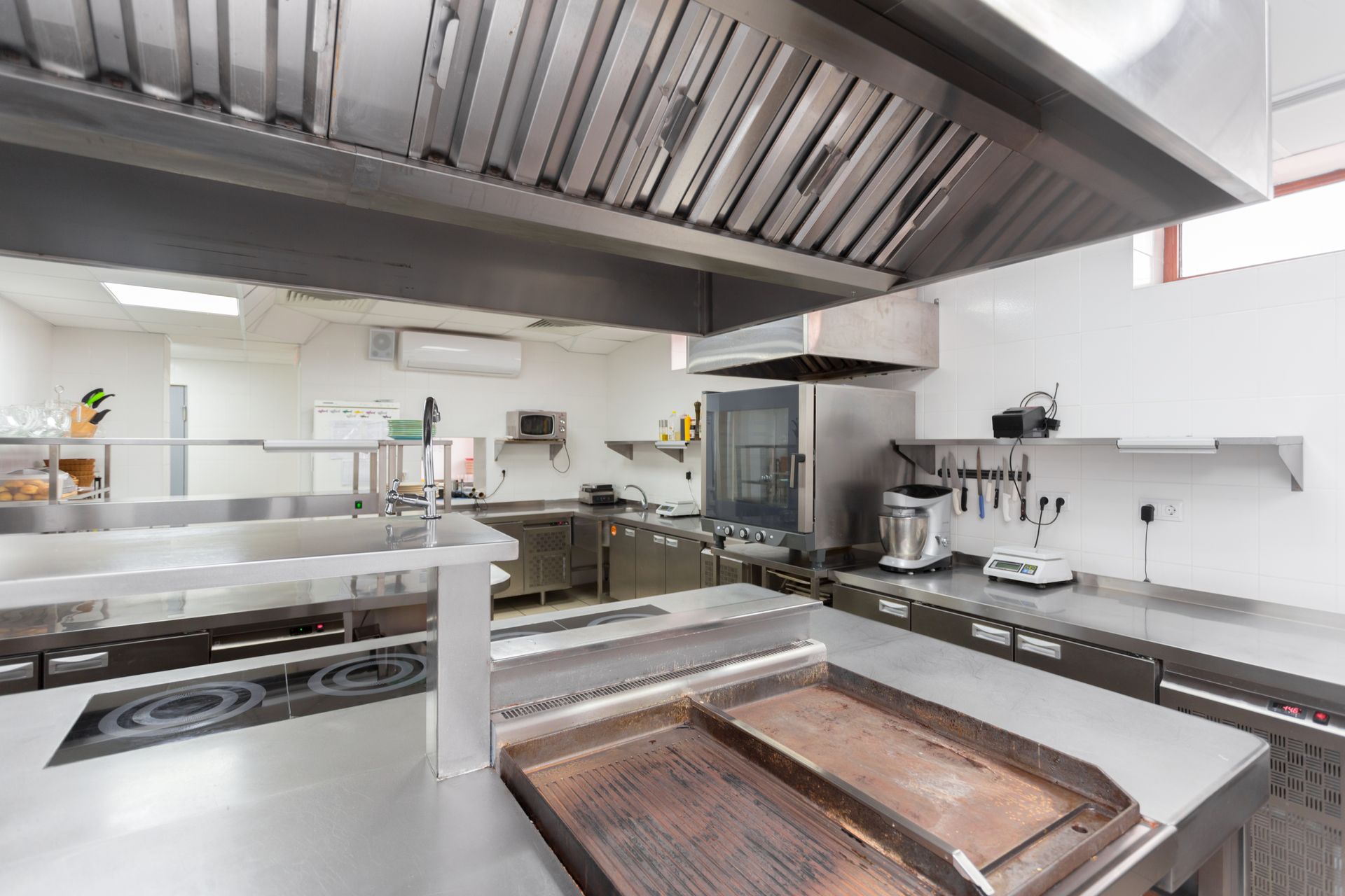 A clean, modern commercial kitchen with stainless steel countertops, a large cooking range, and a ventilation hood.