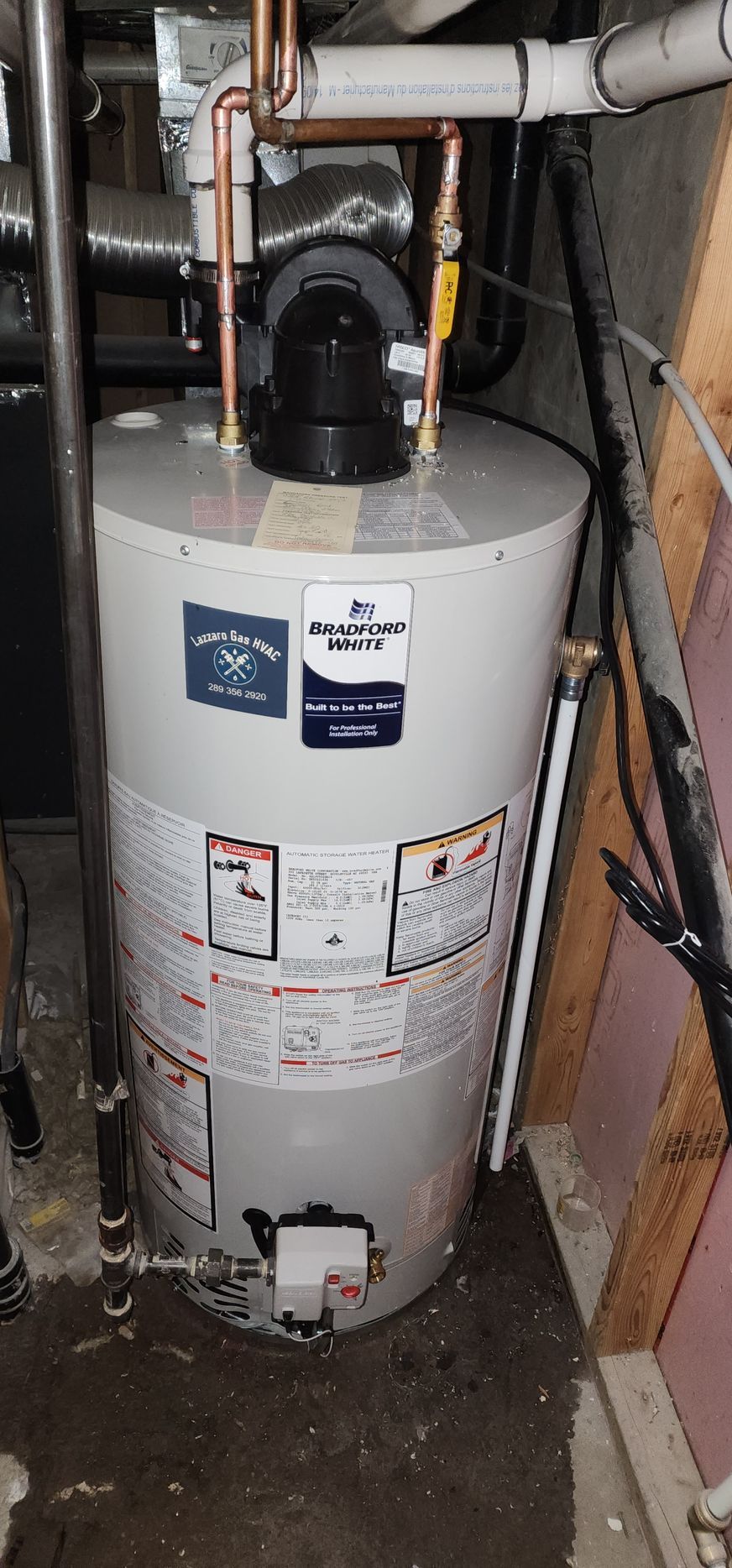 A water heater is sitting in a basement next to a pipe.