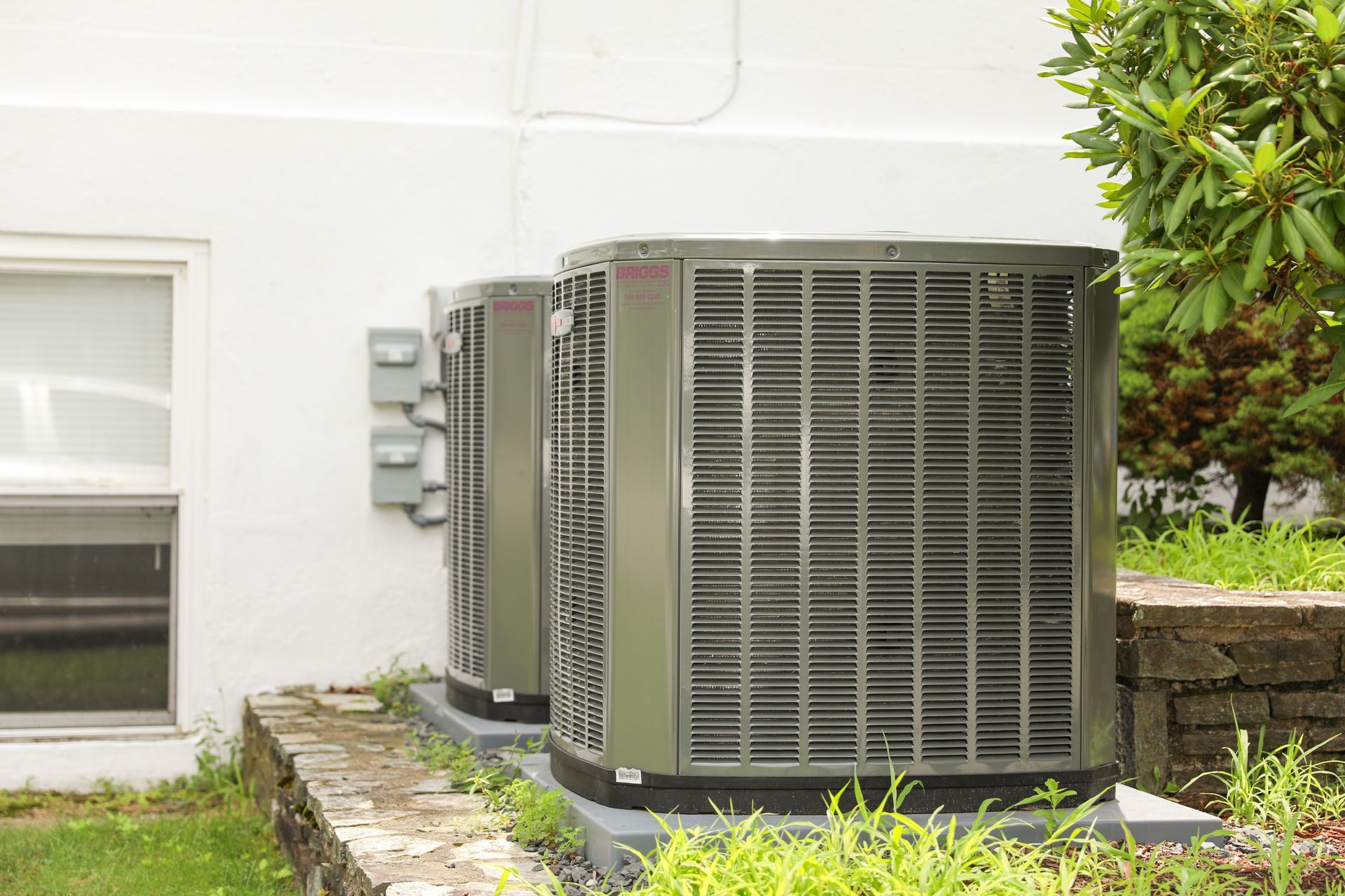 Two outdoor air conditioning units next to a white building.