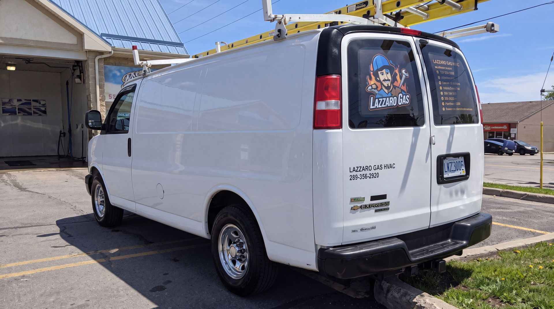 White cargo van parked in a lot, viewed from the rear-left side, with a ladder rack on top.