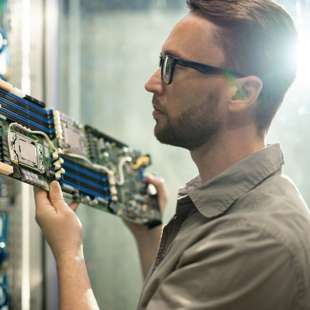 A man wearing glasses is working on a motherboard in a server room.