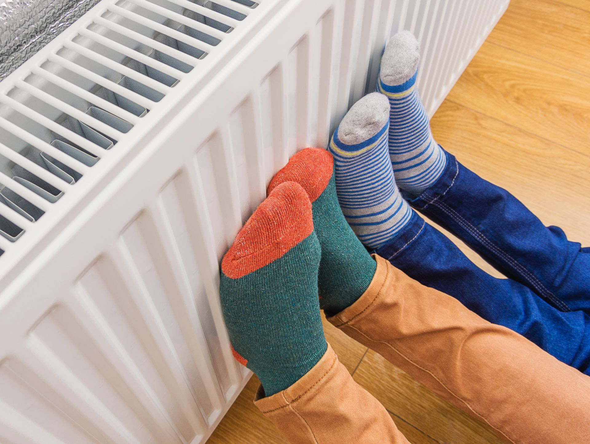 Two people wearing socks are warming their feet on a radiator.