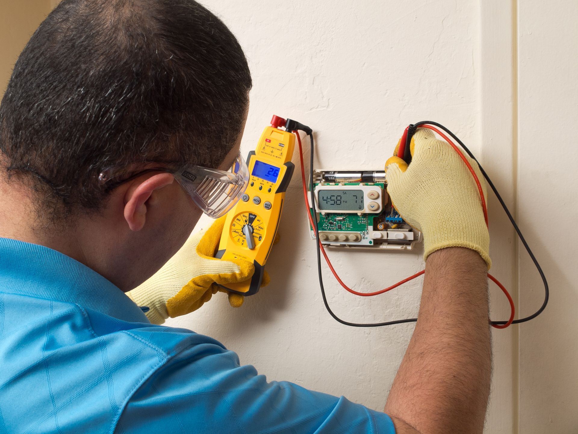 A man is working on a thermostat with a multimeter