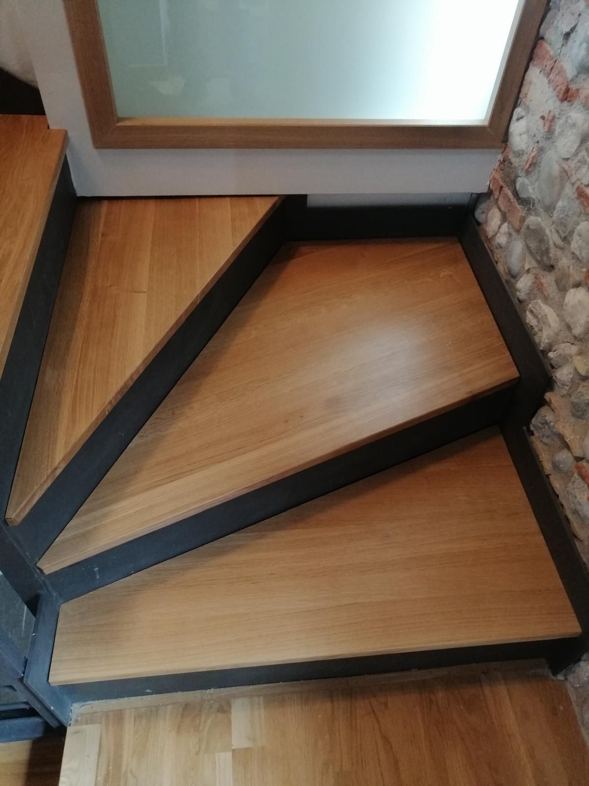 Una scala in legno con struttura in metallo e un muro in pietra sullo sfondo.