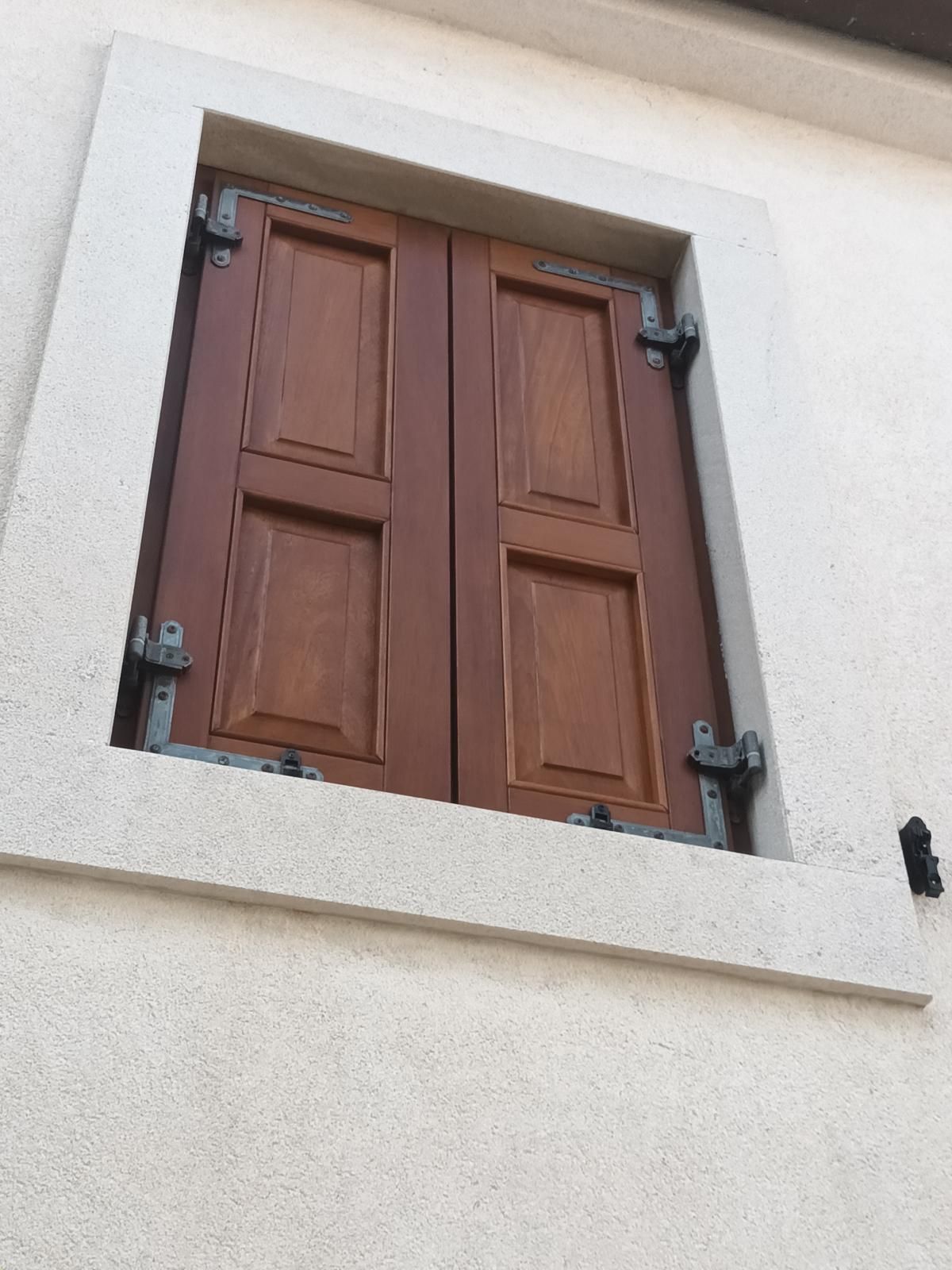 Una finestra con persiane in legno su un muro bianco