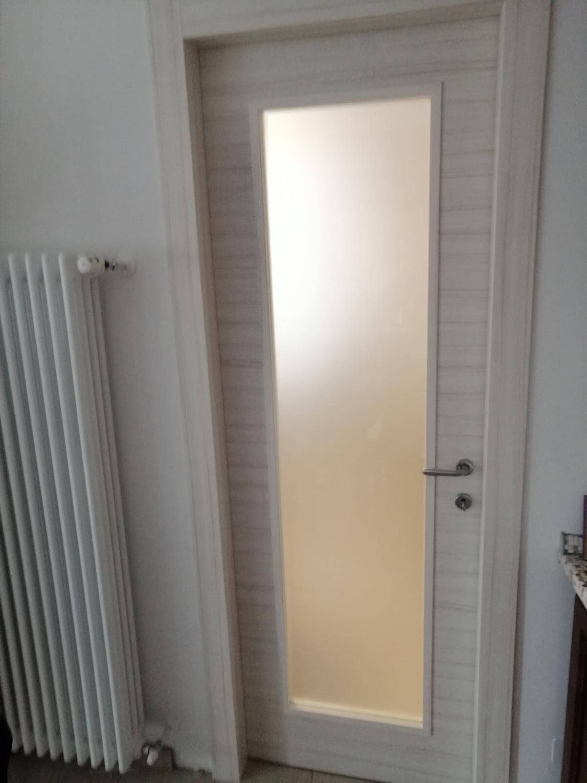 Una porta bianca con una finestra di vetro in una stanza accanto a un termosifone.