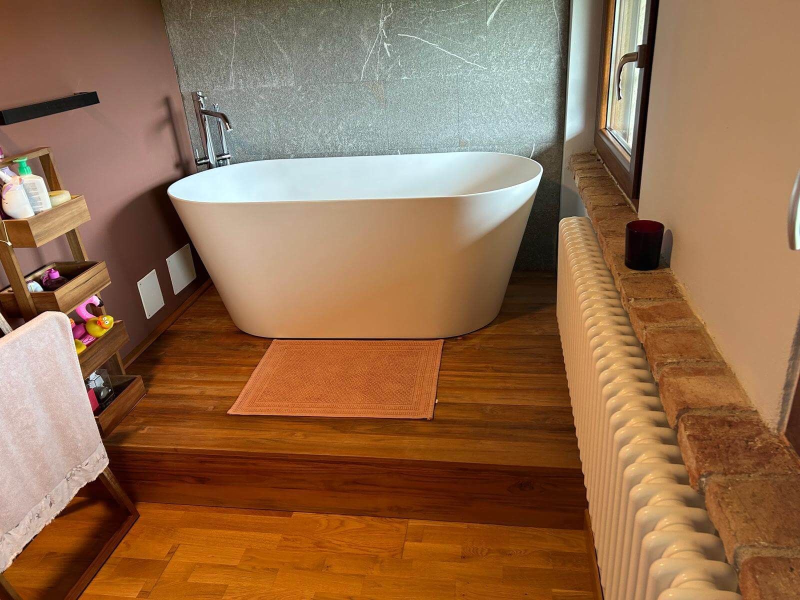 Una vasca da bagno è appoggiata su un pavimento di legno in un bagno accanto a un termosifone.